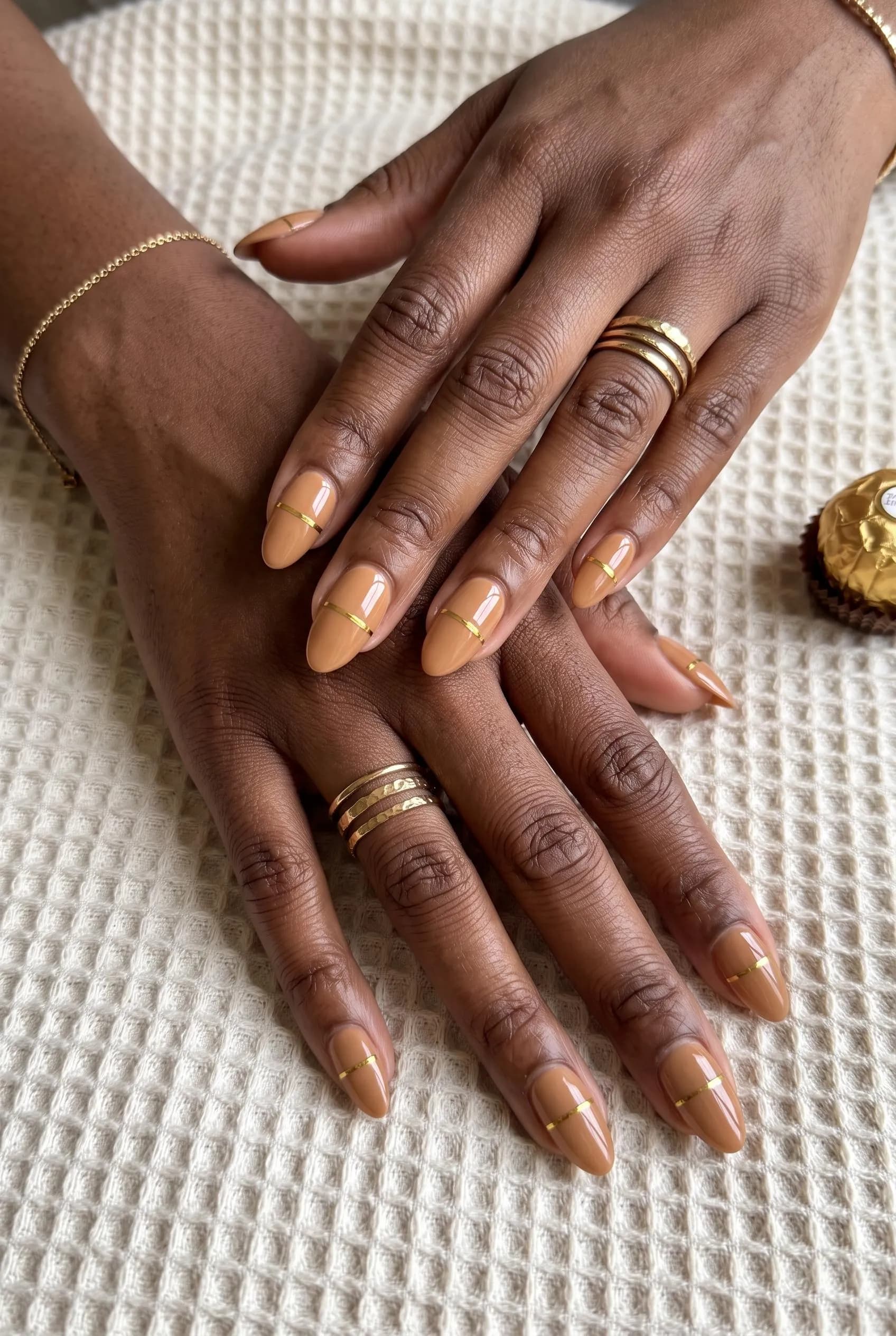 Light caramel almond nails with a thin gold line across each tip on deep brown skin