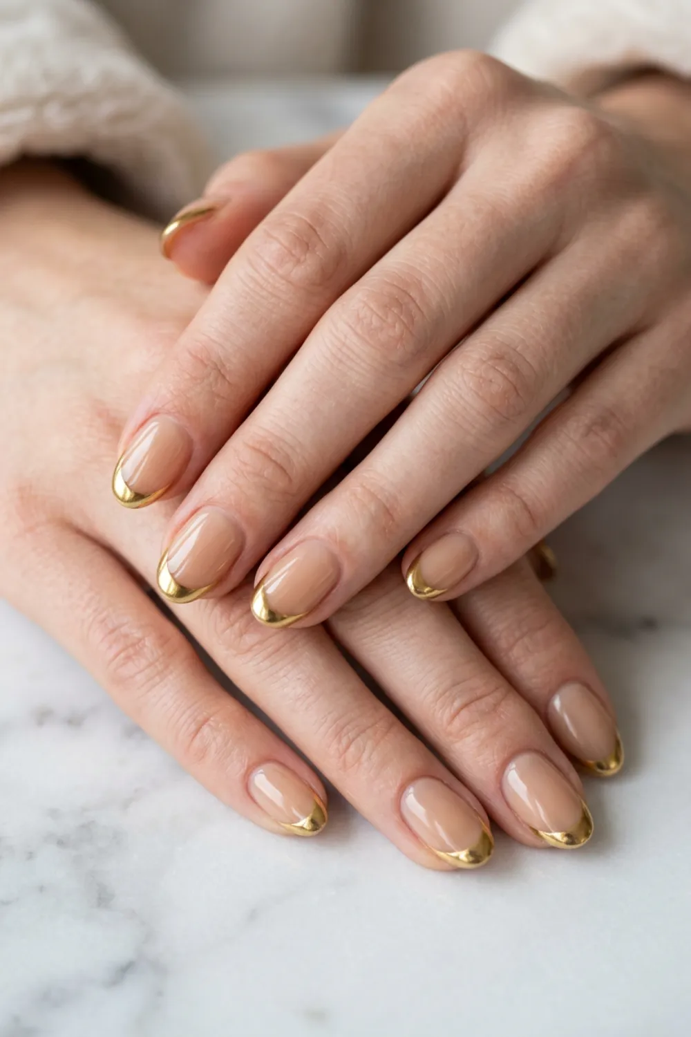 Short oval nails in a beige nude with thin gold French tips