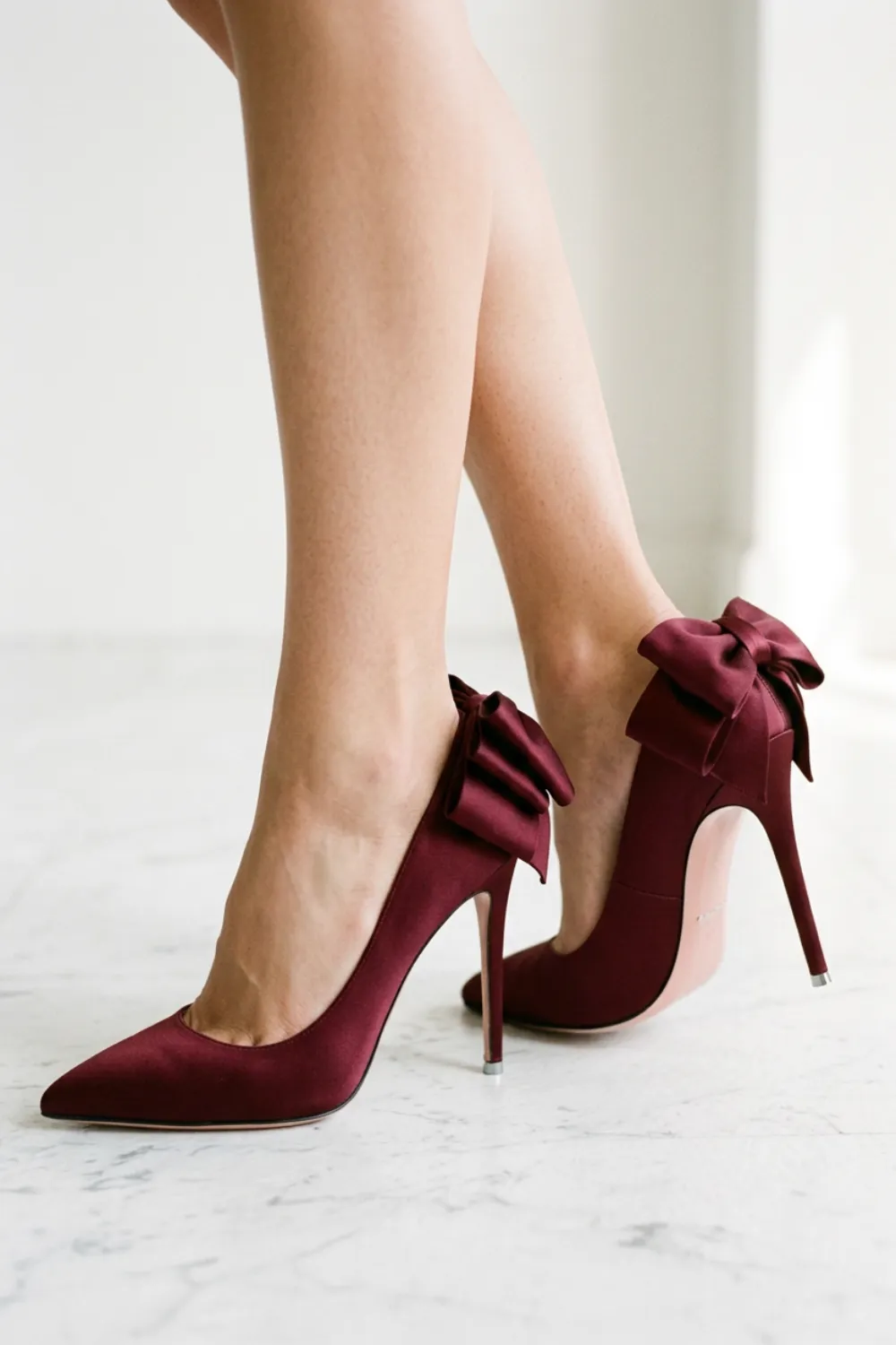 Burgundy satin pumps with bows at the heel, shown in a close-up