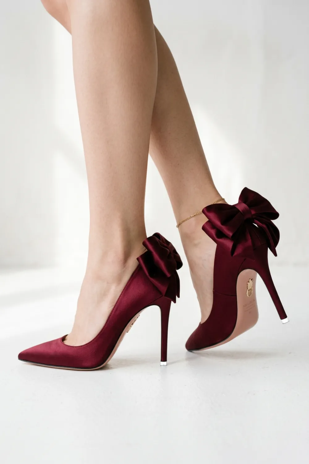 Burgundy satin stiletto pumps with large bows at the back of the heel
