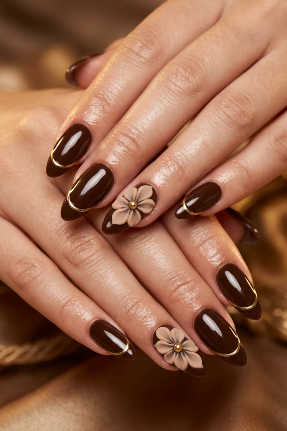 Glossy dark chocolate almond nails with gold outline tips and a 3D beige flower