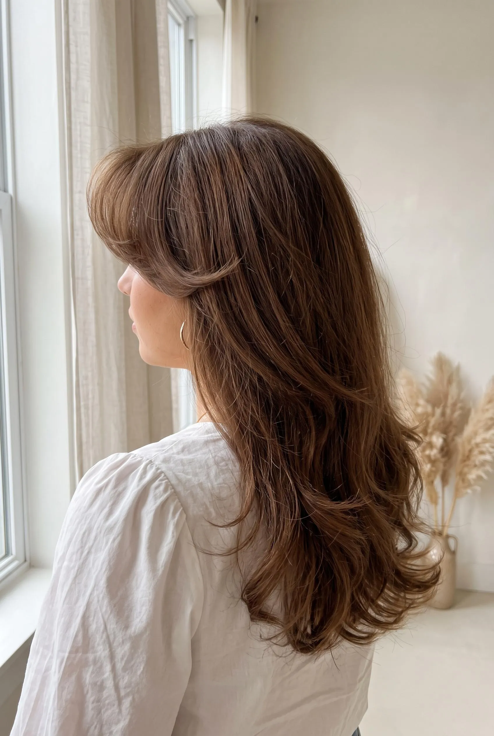 Long chestnut brown blowout with teased 80s curtain bangs swept back from the face