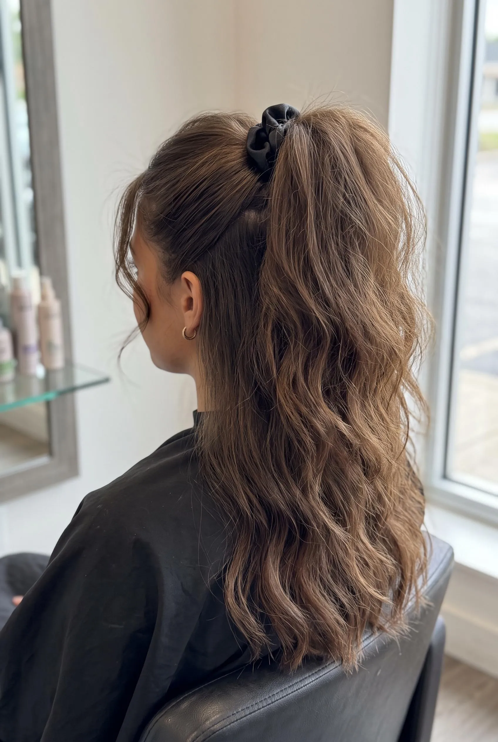 Teased 80s high ponytail with a black scrunchie and a full wavy tail in a salon chair