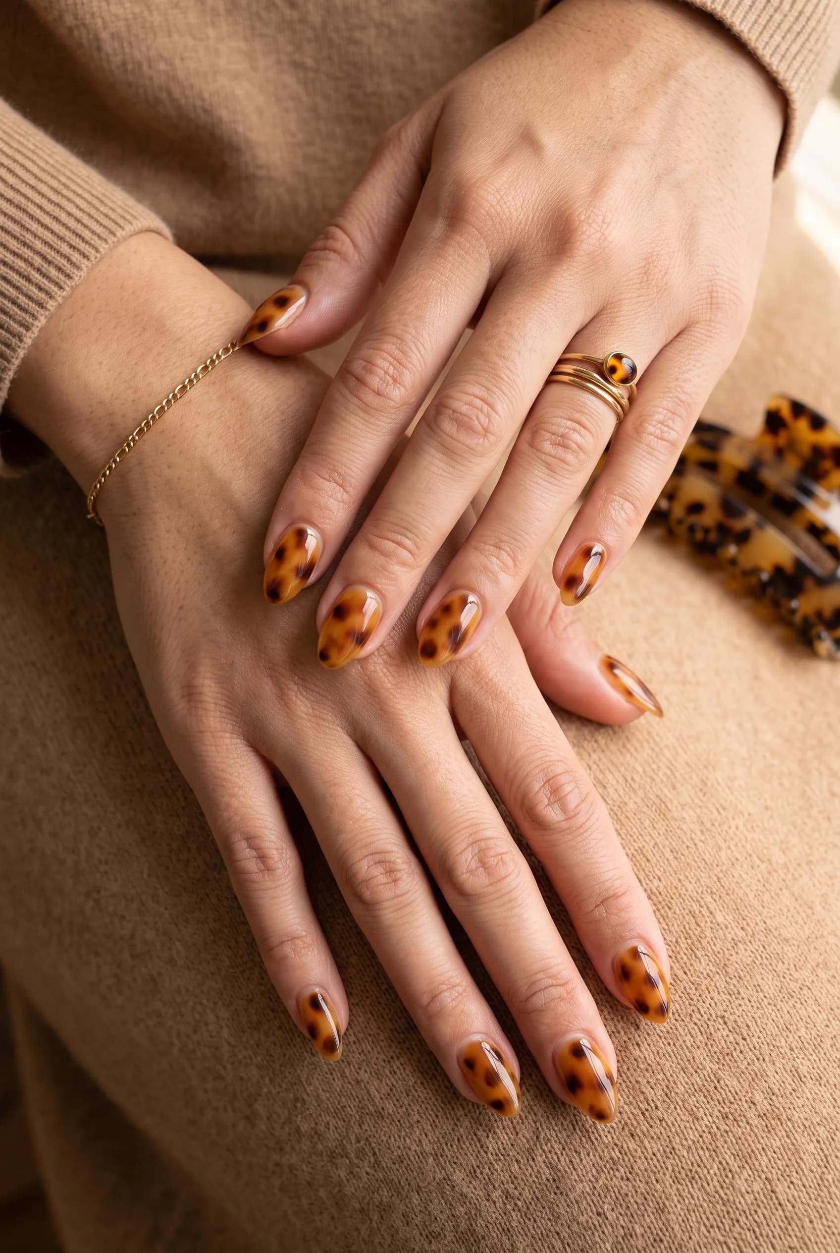 Glossy amber and black tortoiseshell almond nails on a camel knit