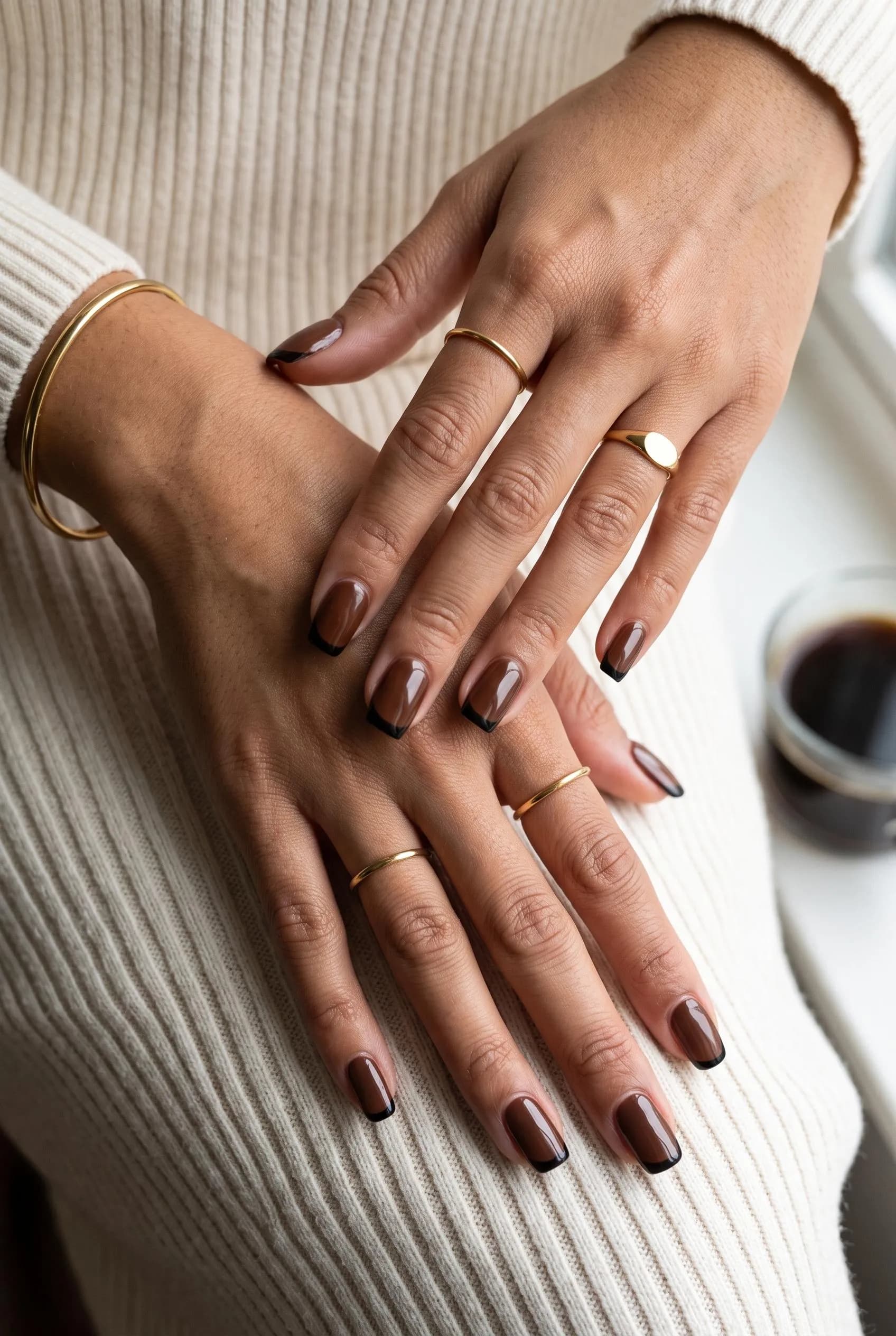 Chocolate brown nails with thin black French tips on a cream knit