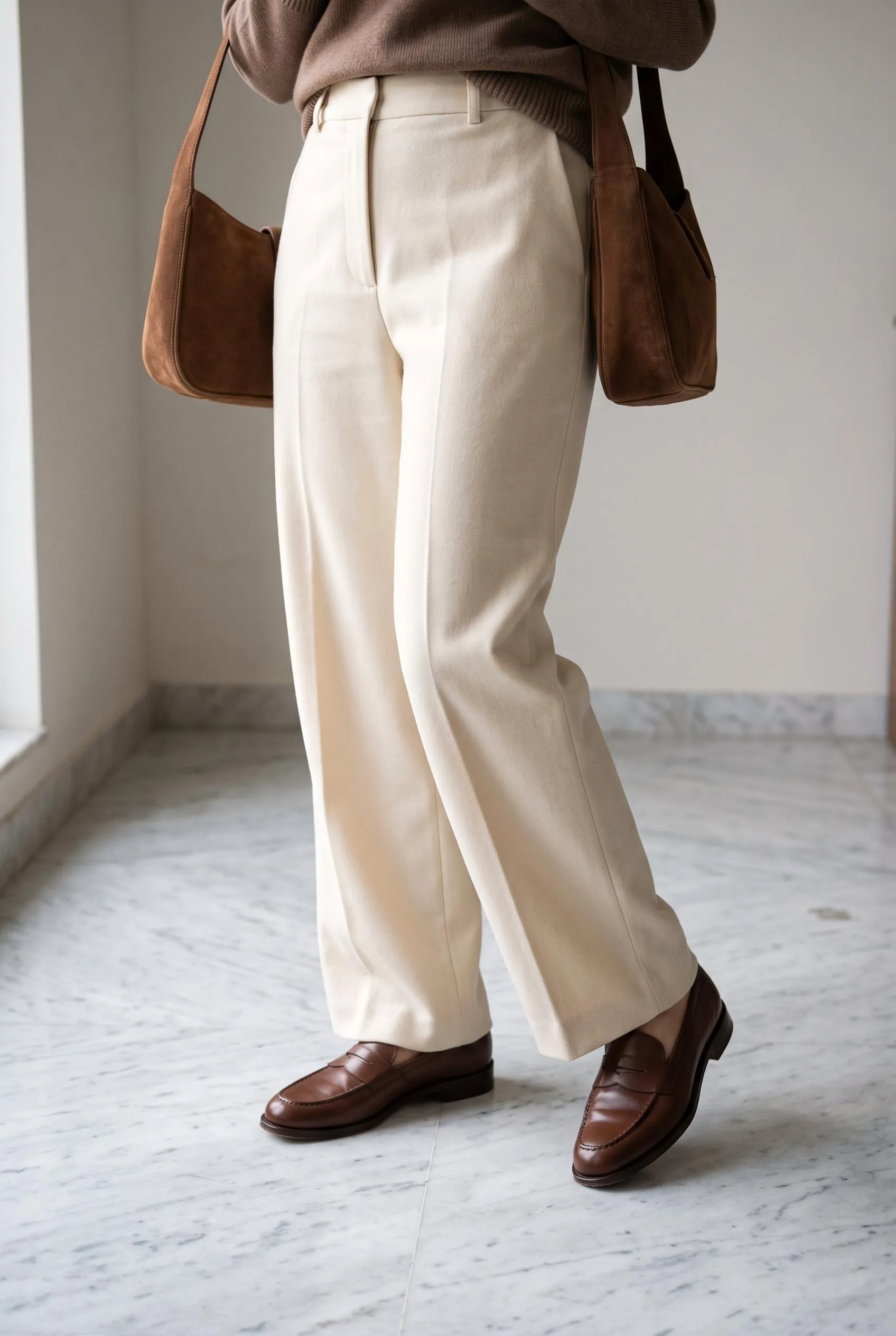 Chocolate brown penny loafers with cream wide-leg trousers and a brown suede bag