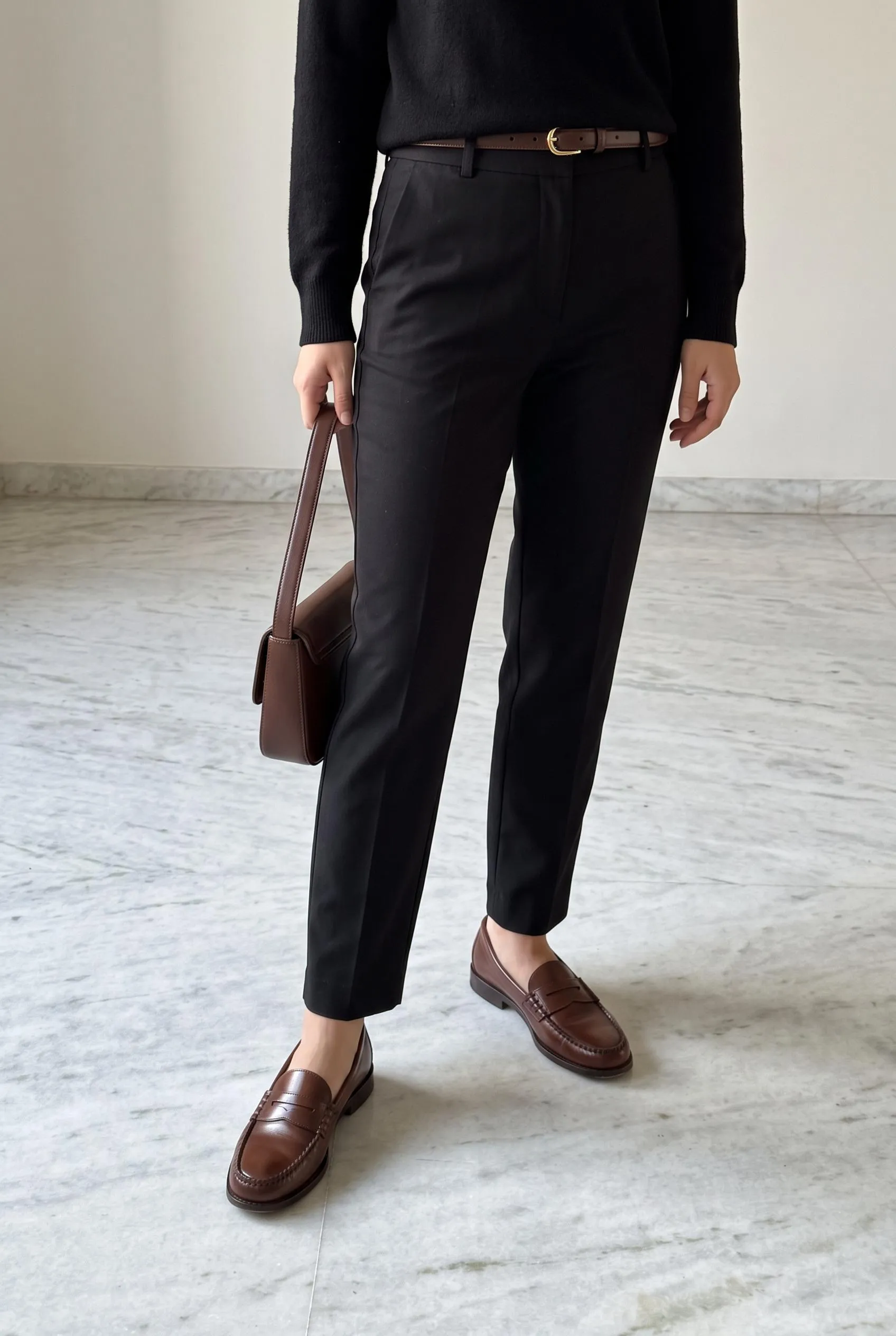 Brown penny loafers with black trousers, a black knit and a brown belt and bag
