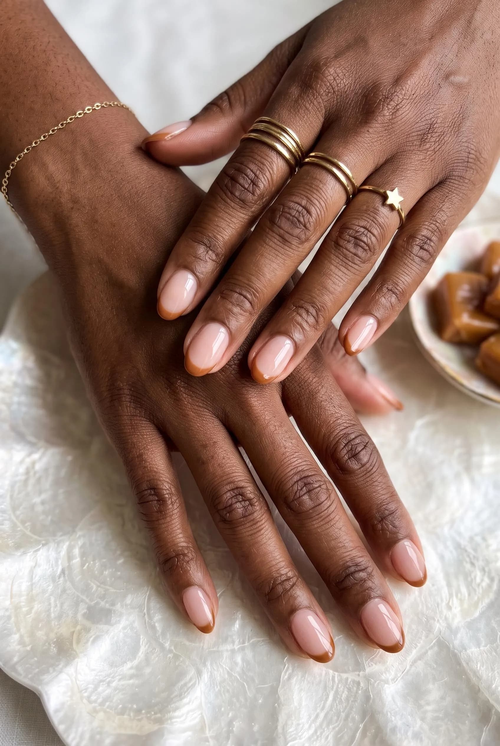 Sheer nude oval nails with thin caramel French tips on deep brown skin