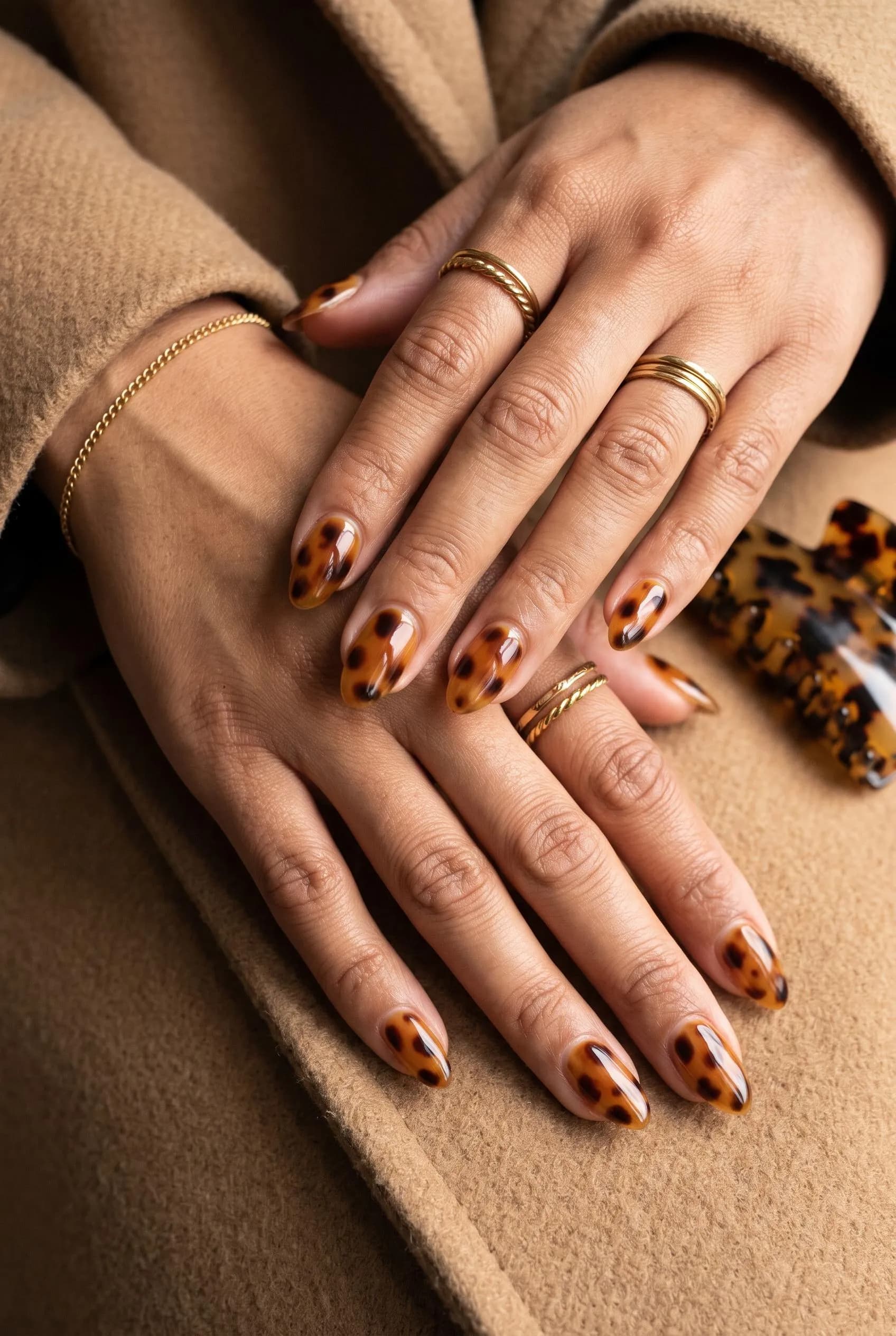 Glossy amber tortoiseshell almond nails on a camel coat