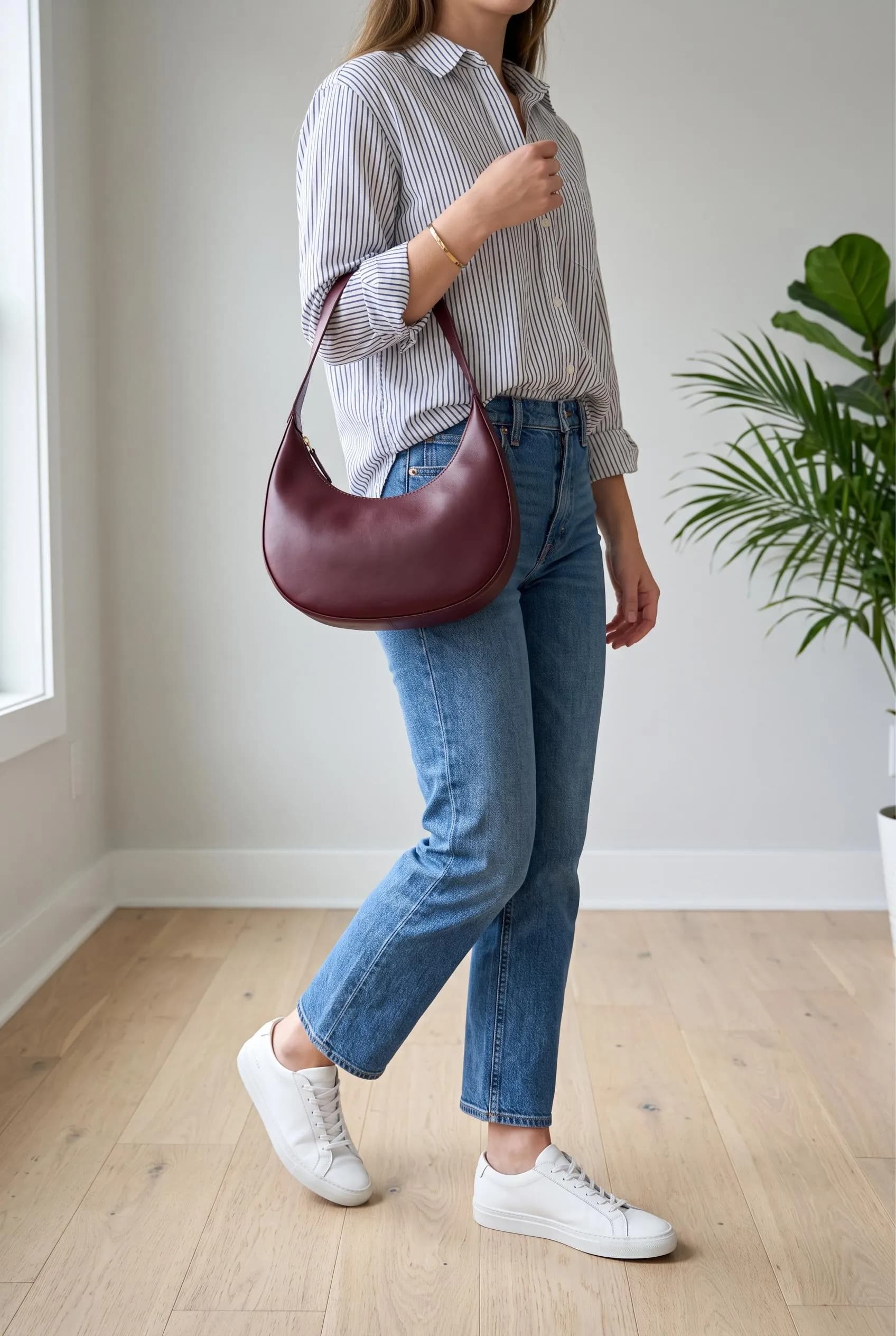 Burgundy crescent shoulder bag with a striped shirt, straight blue jeans and white sneakers