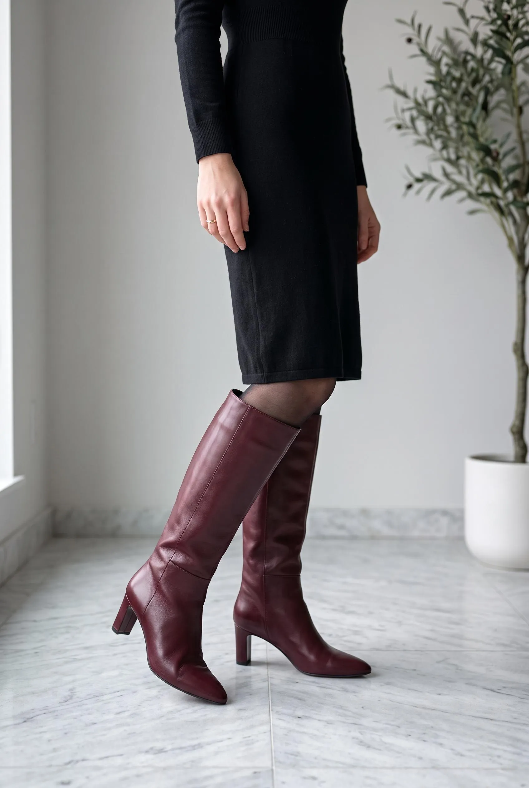 Burgundy leather knee-high boots with a black knit dress and sheer black tights