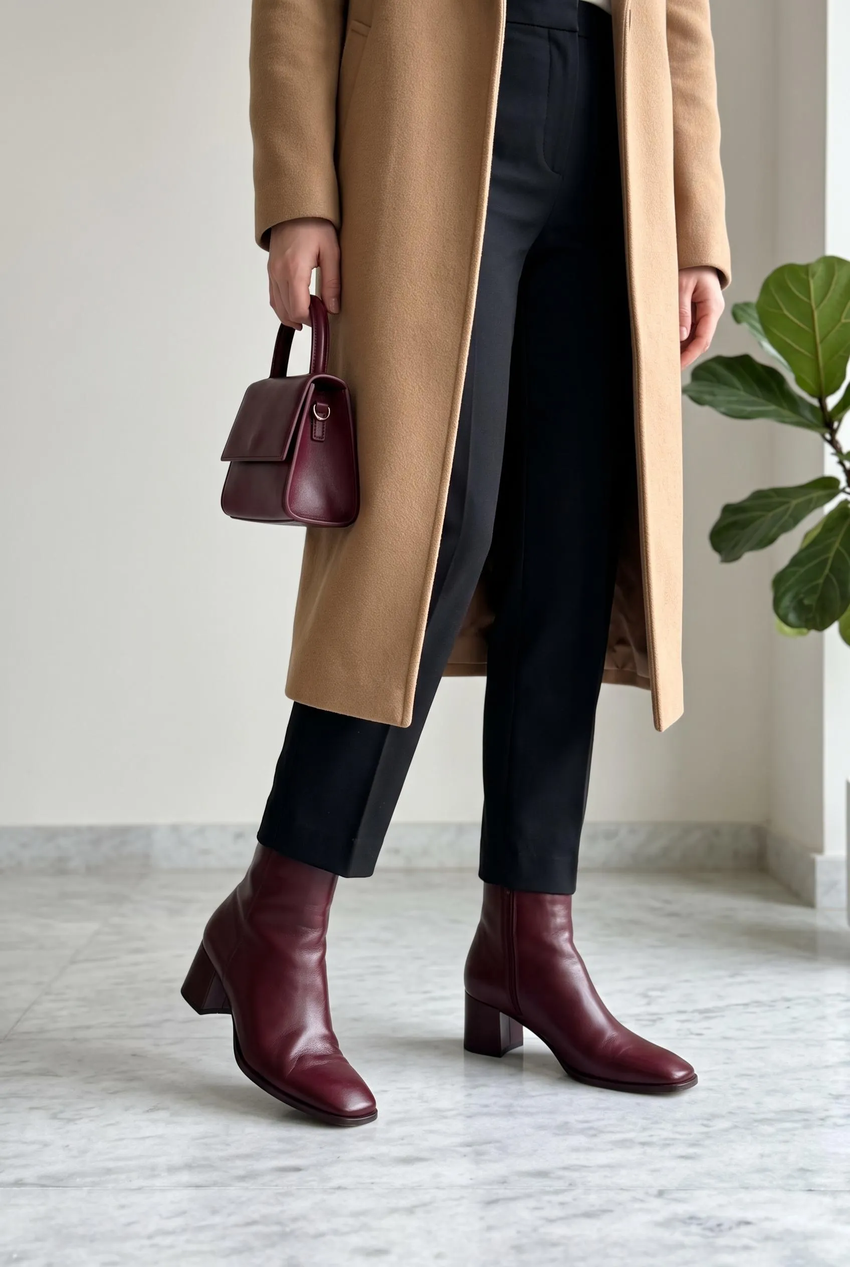 Burgundy ankle boots with cropped black trousers, a camel coat and a matching burgundy bag