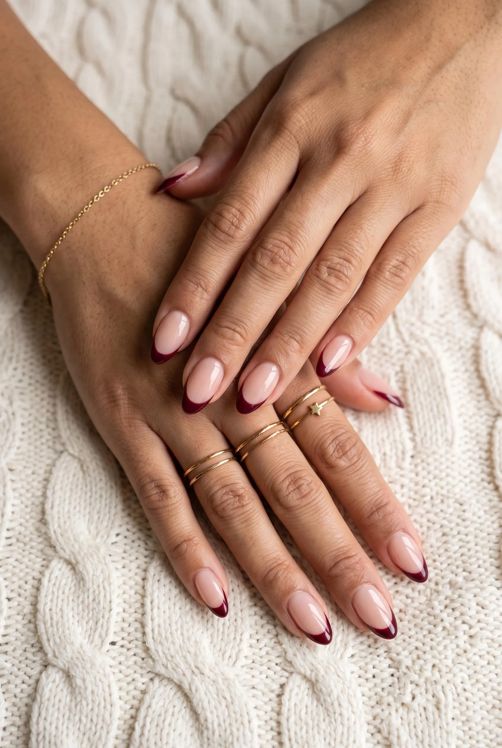 Nude almond nails with thin burgundy French tips on a cream knit