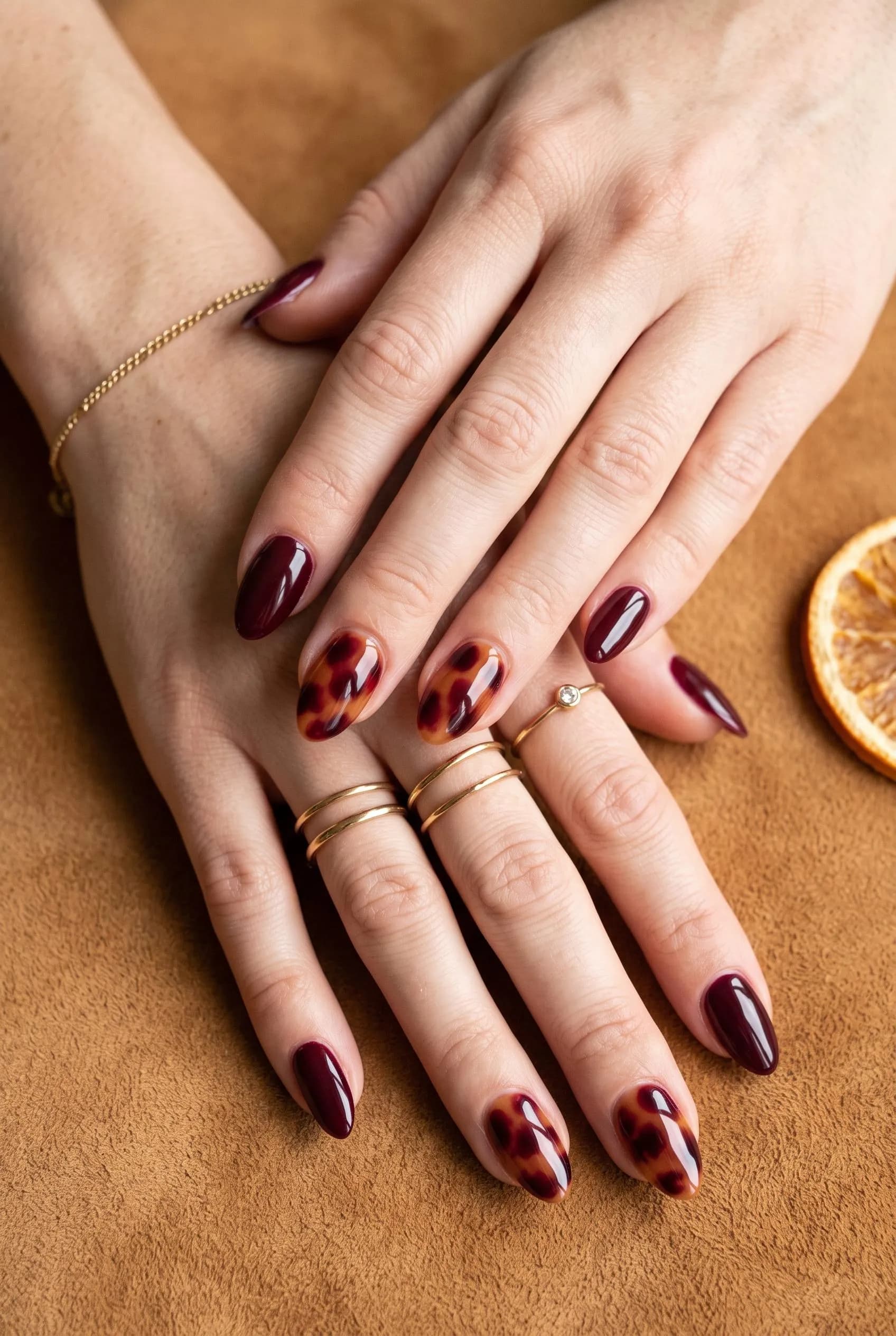 Burgundy nails with burgundy and amber tortoiseshell accent nails on caramel suede