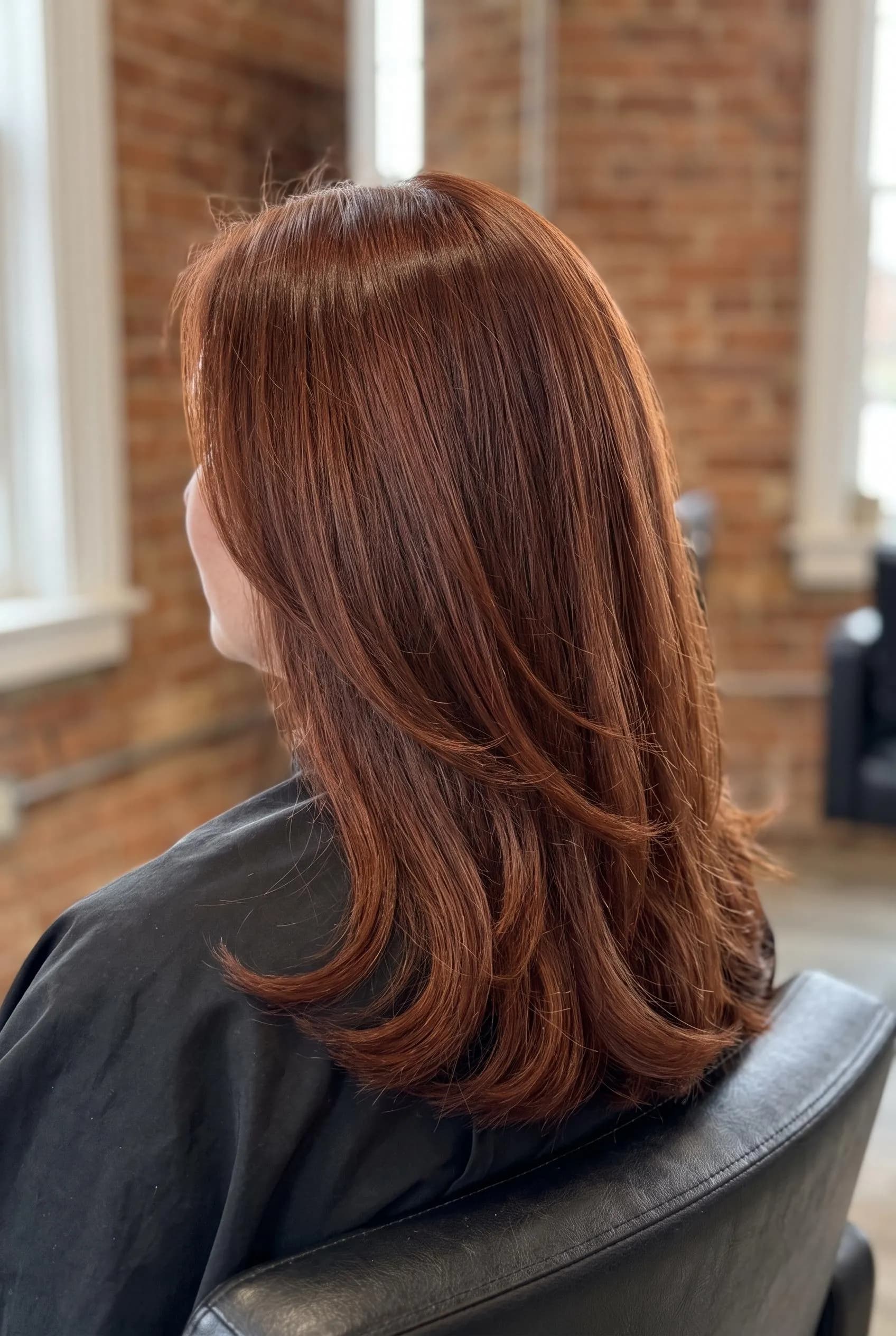 Shoulder-length layered auburn hair in a salon chair
