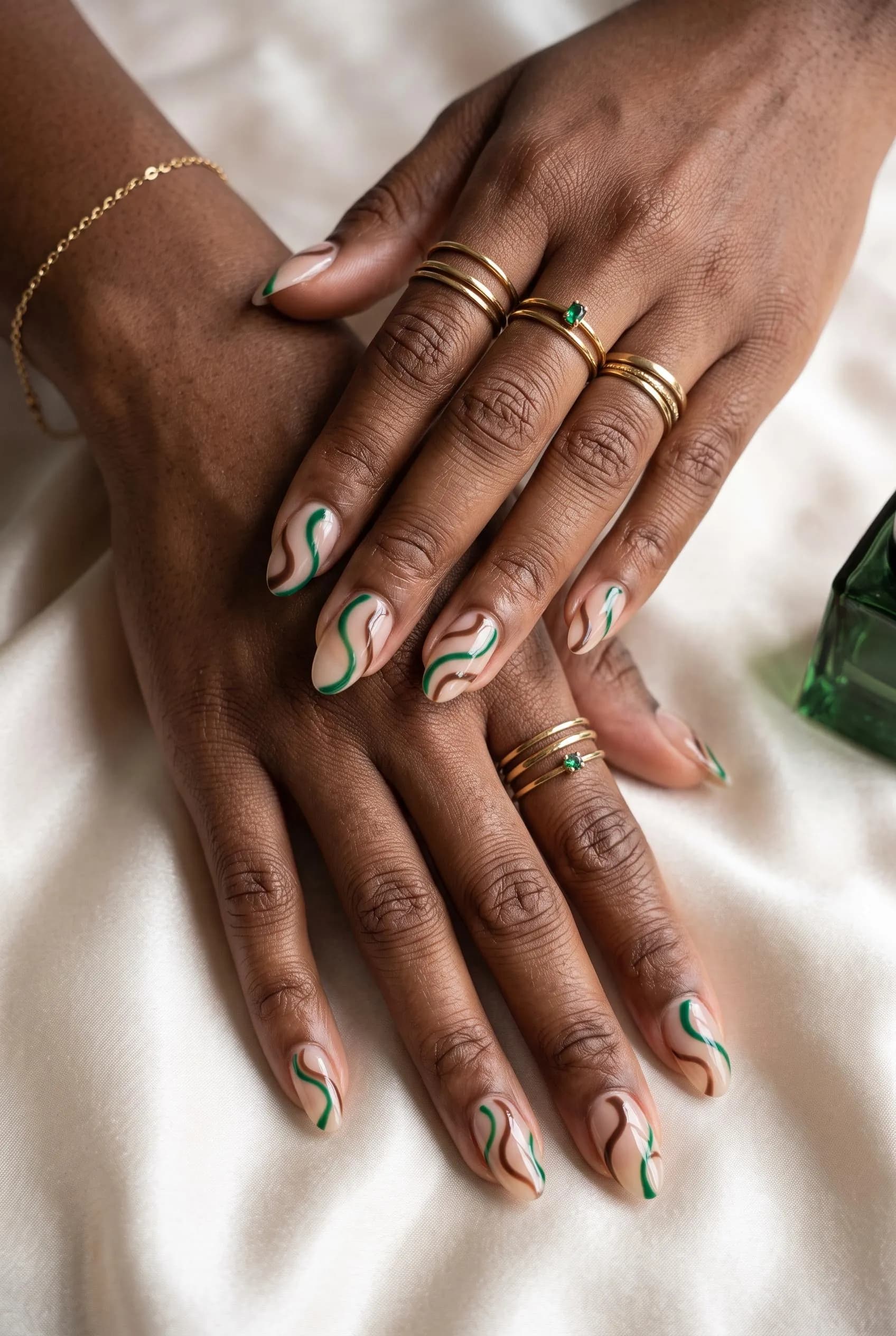 Sheer nude almond nails with thin emerald and brown swirls on deep brown skin
