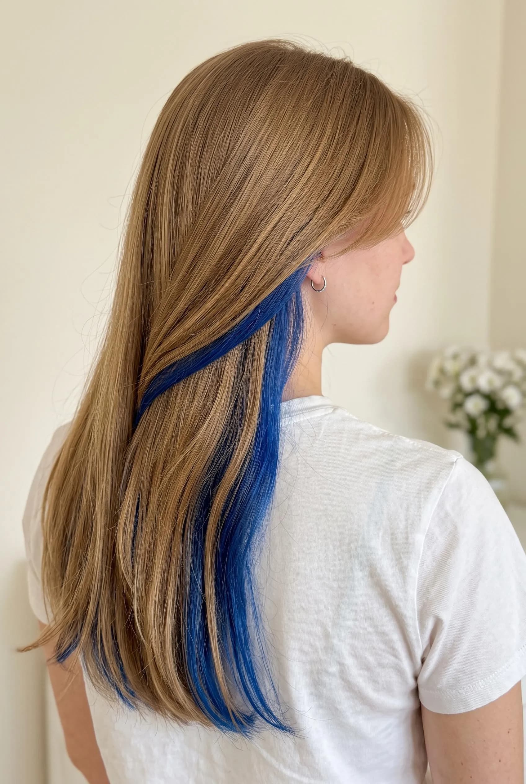 Long light brown hair with a bright royal blue peekaboo underlayer swept over one shoulder