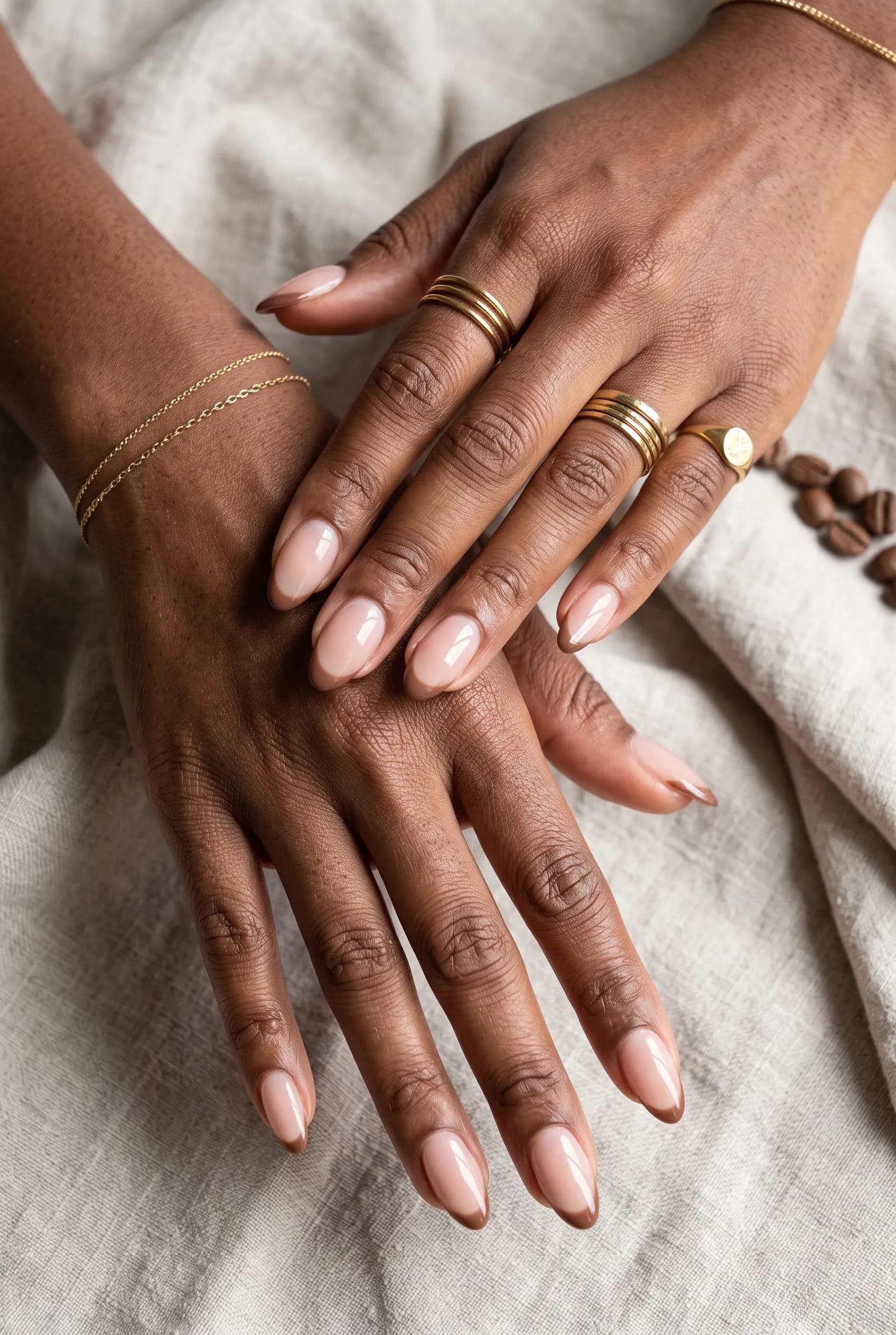 Sheer nude almond nails with thin mocha French tips on deep brown skin