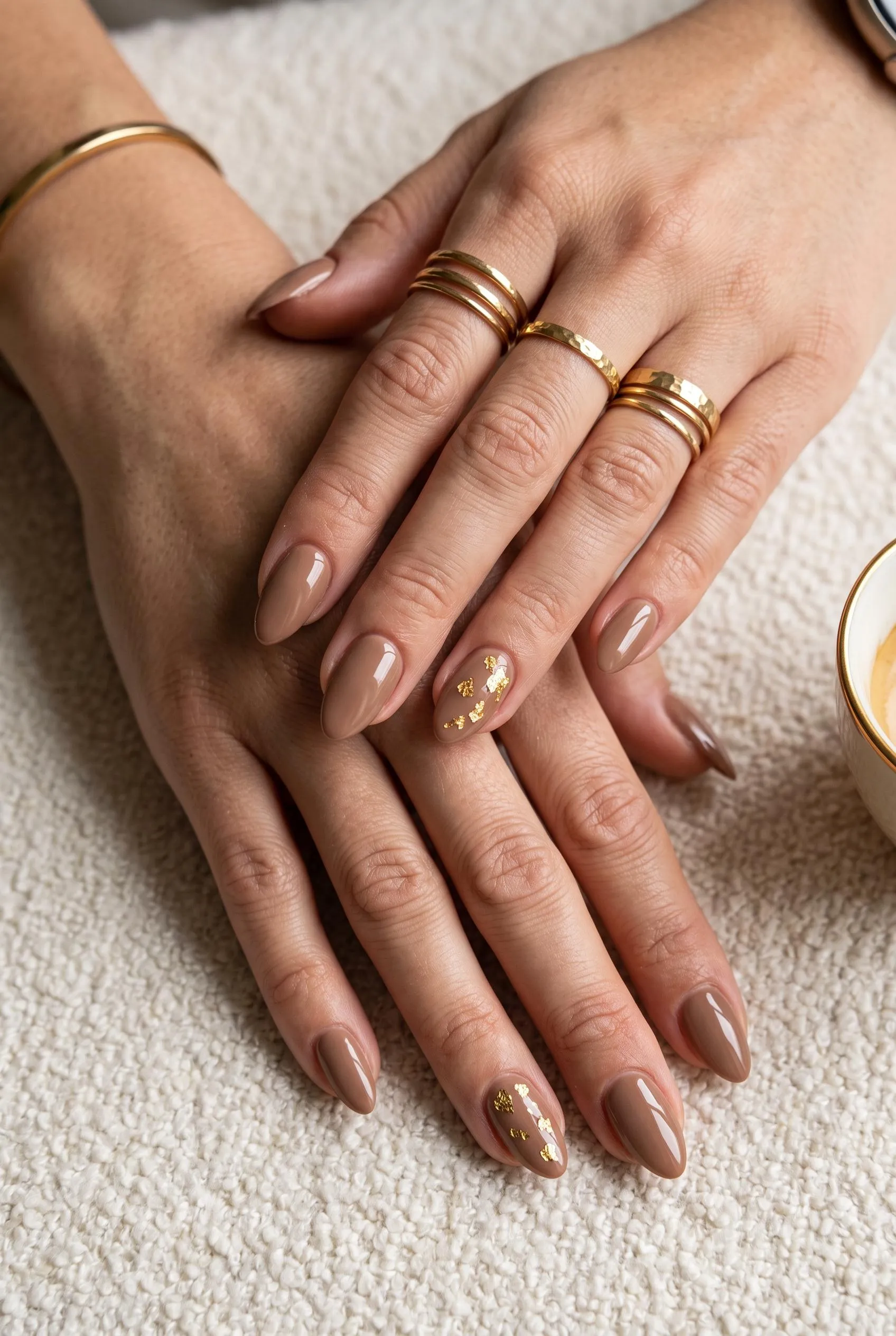 Glossy mocha nails with gold foil flakes on the ring fingers