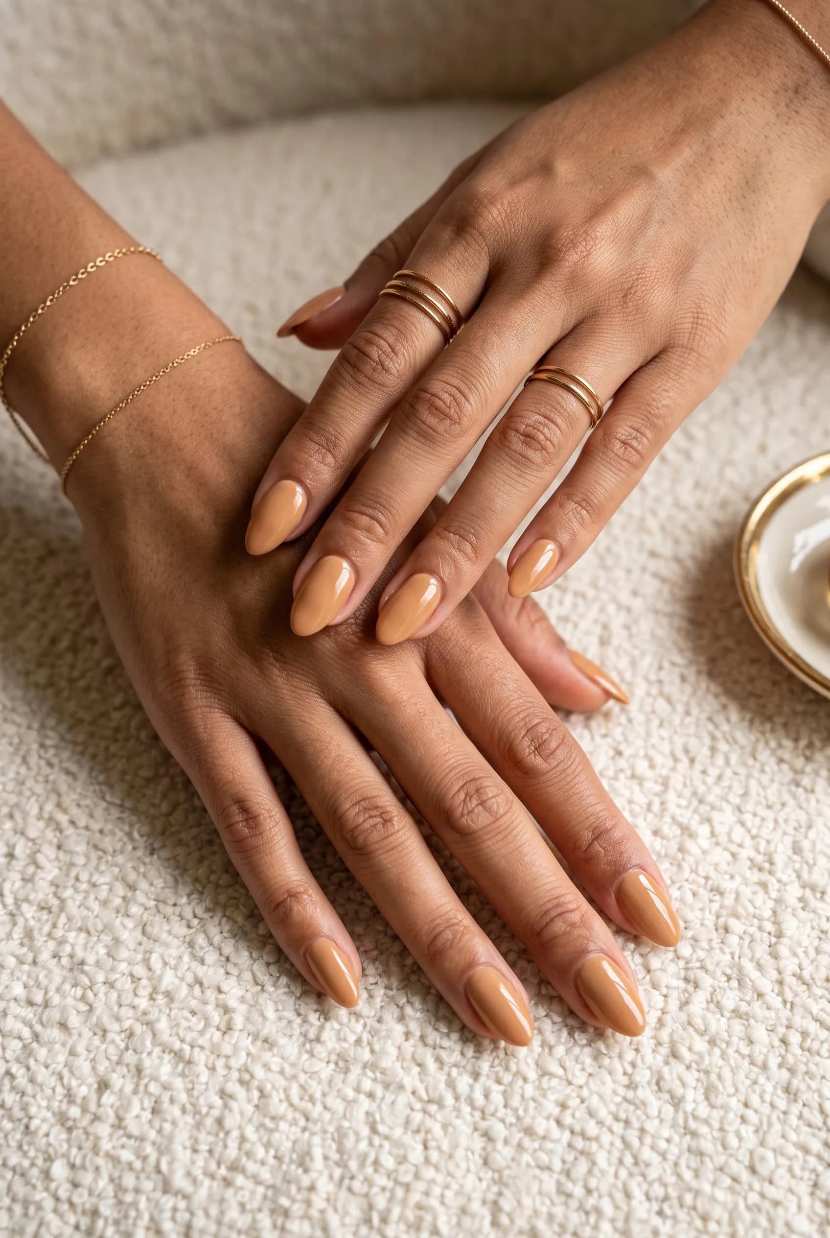 Warm caramel nude almond nails on medium brown skin with gold rings