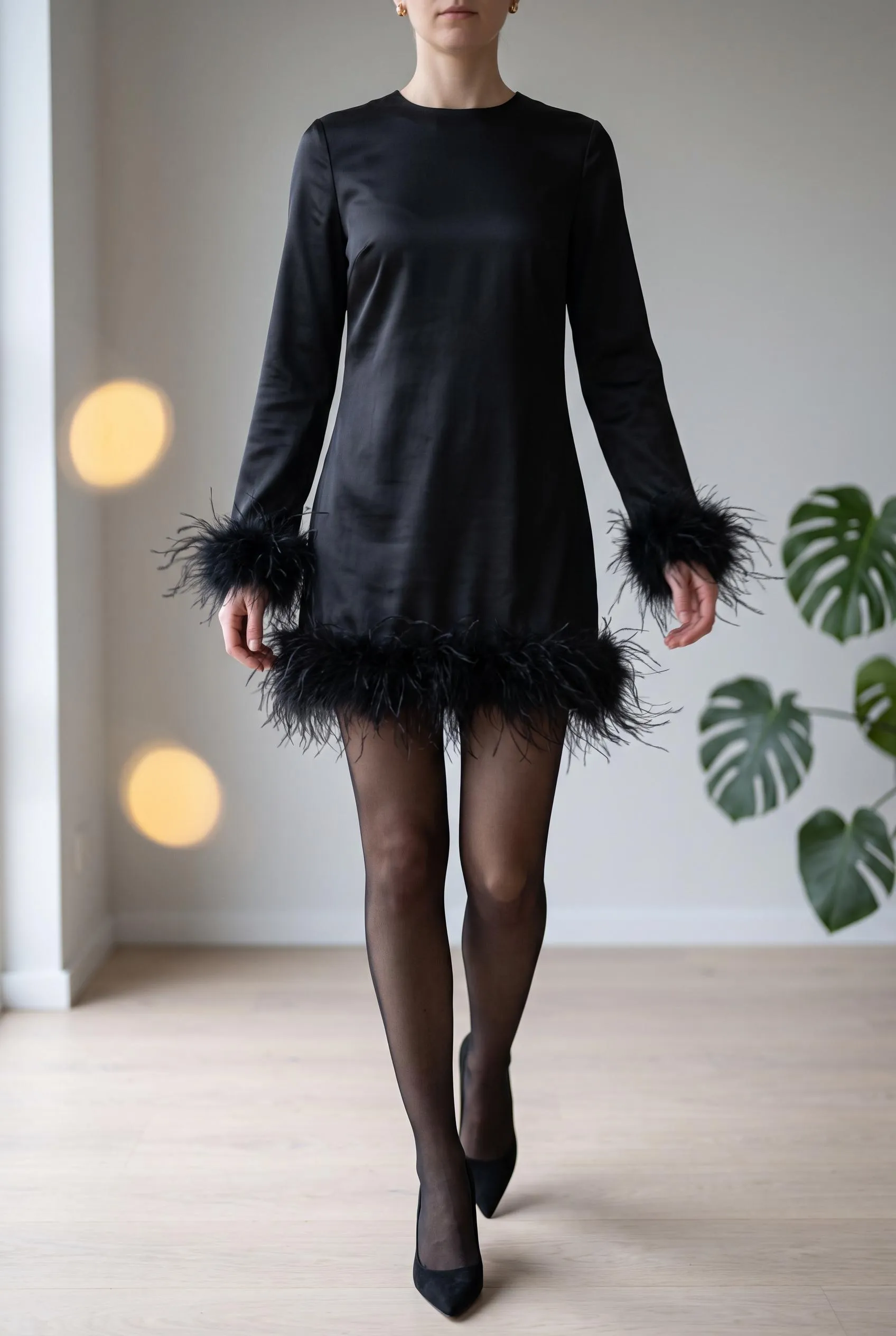 Black satin mini dress with feather trim at the hem and cuffs, sheer tights and heels