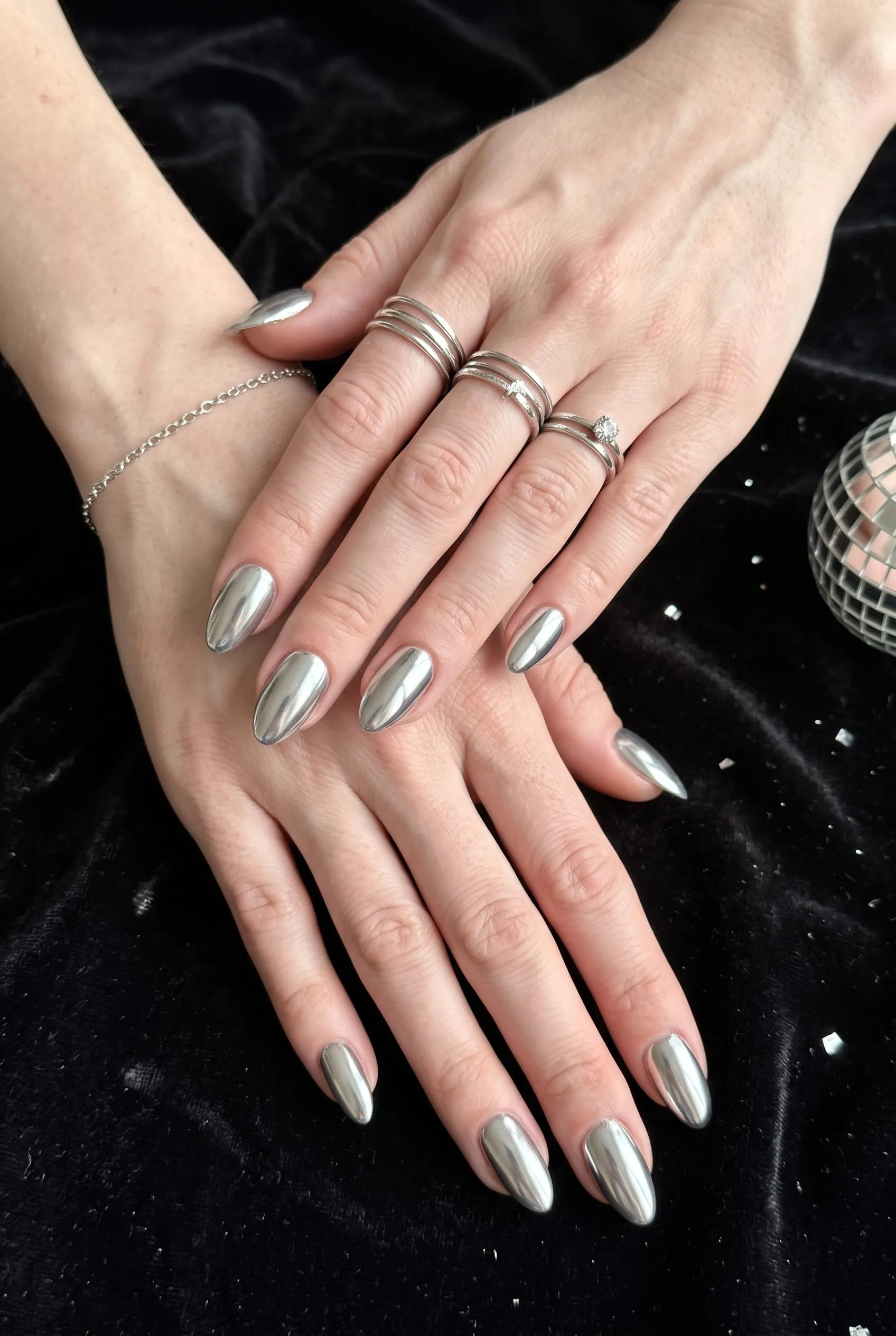 Mirror silver chrome almond nails on black velvet beside a disco ball