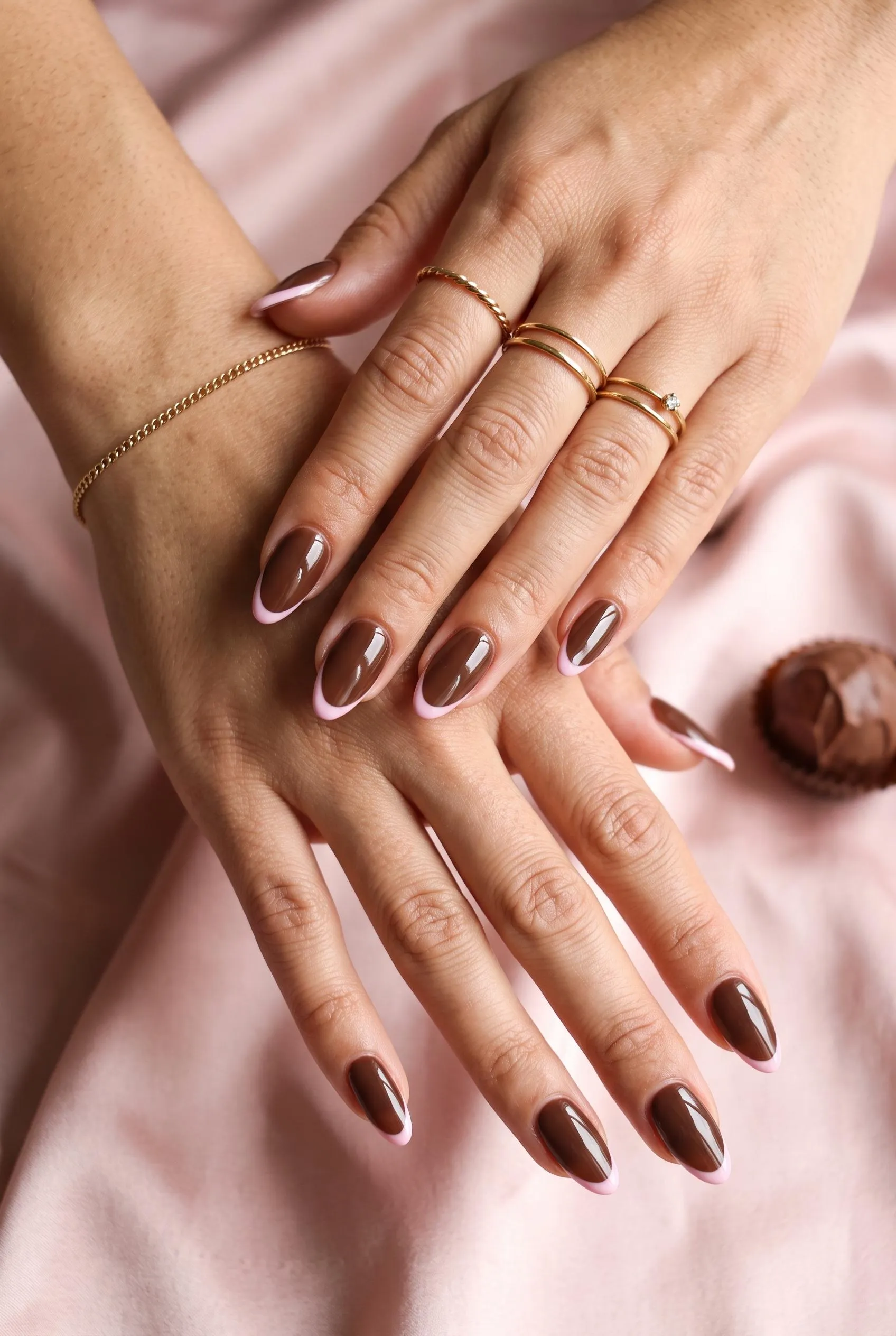 Glossy chocolate brown almond nails with thin baby pink French tips on blush satin
