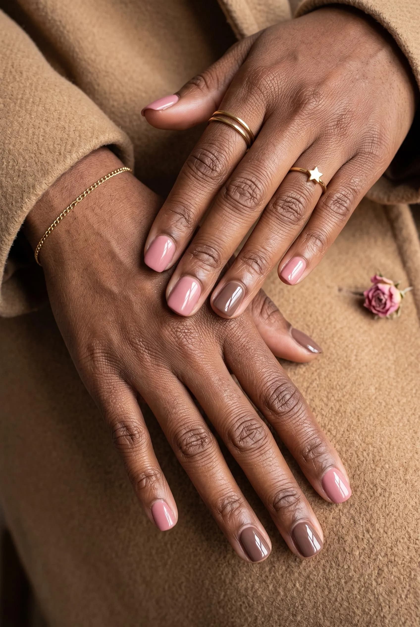 Short nails alternating dusty pink and mocha brown on deep brown skin over a camel coat