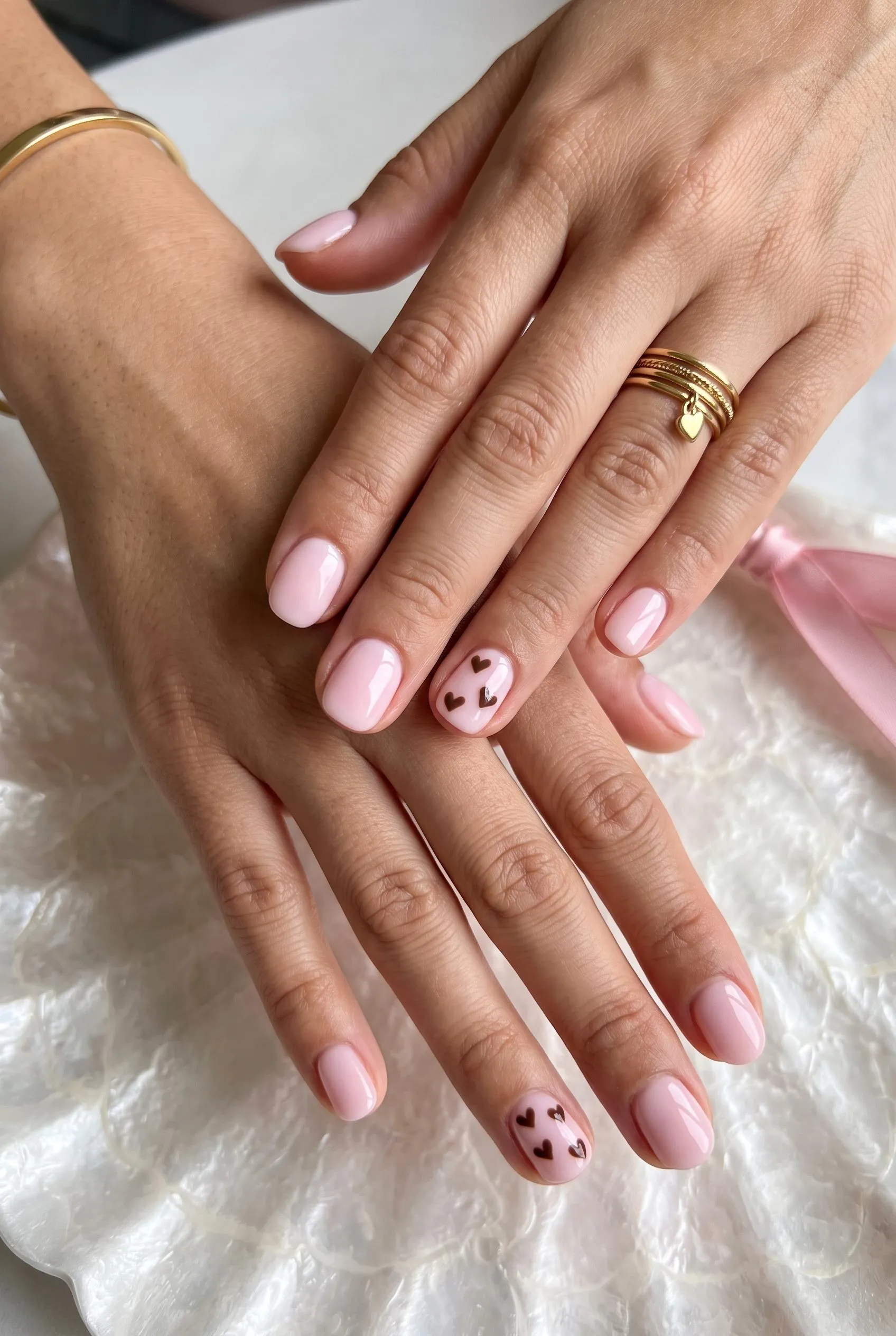 Milky pink nails with tiny chocolate brown hearts on the ring fingers