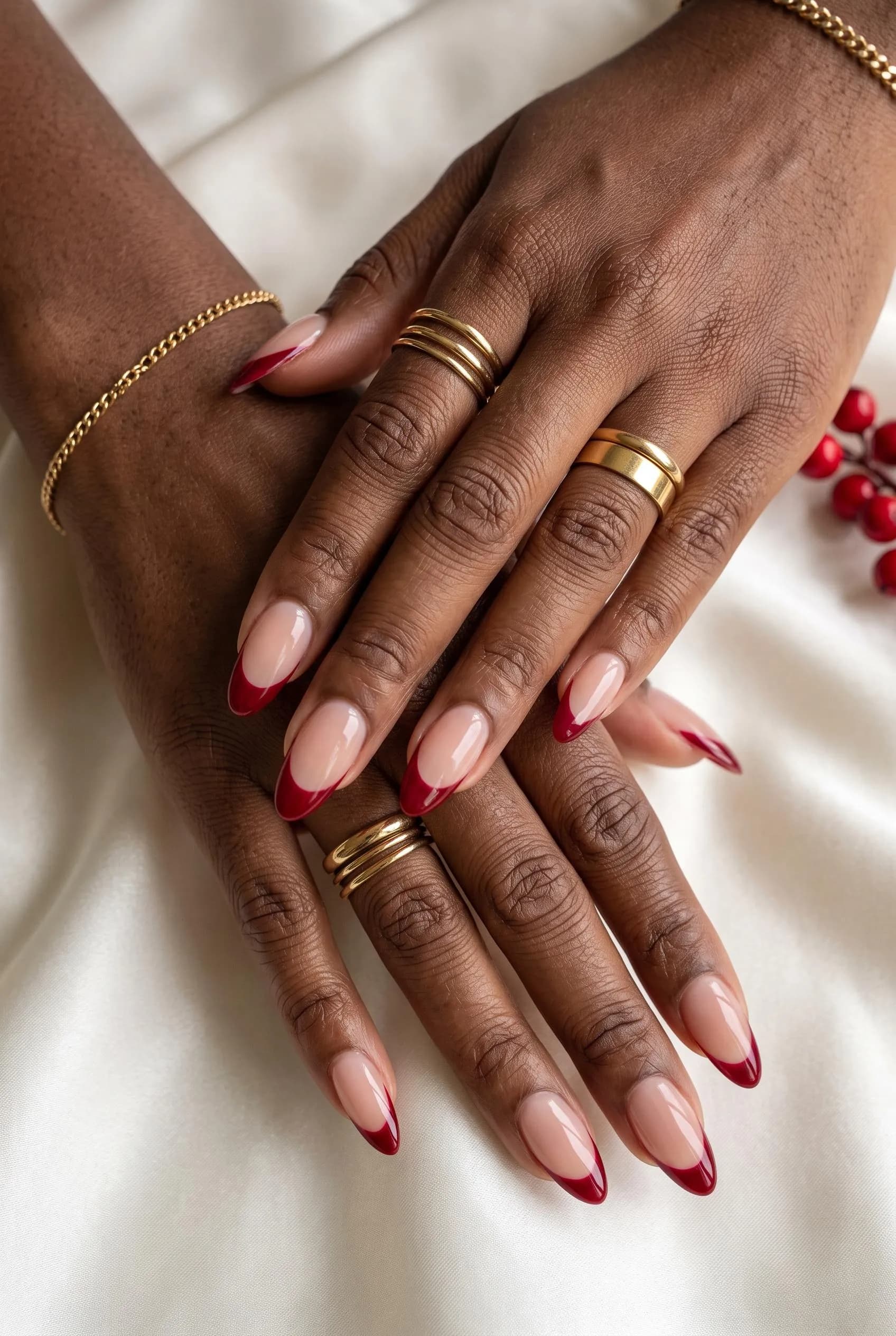 Long almond nails with a sheer nude base and deep red French tips on deep brown skin