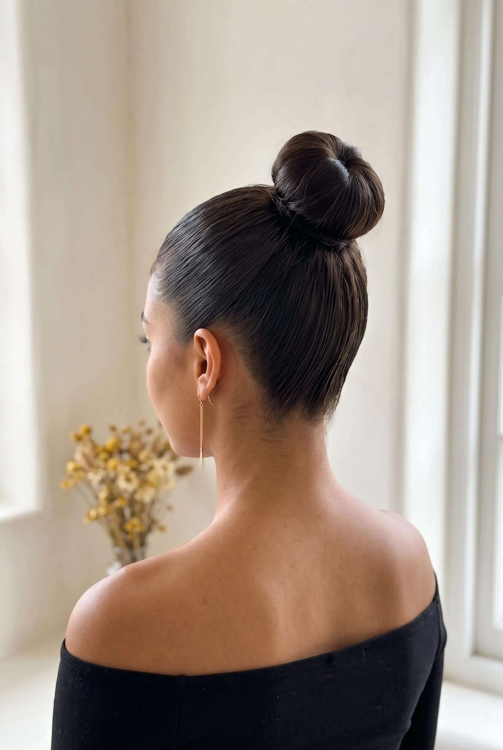 High sleek bun on the crown with a black off-the-shoulder top