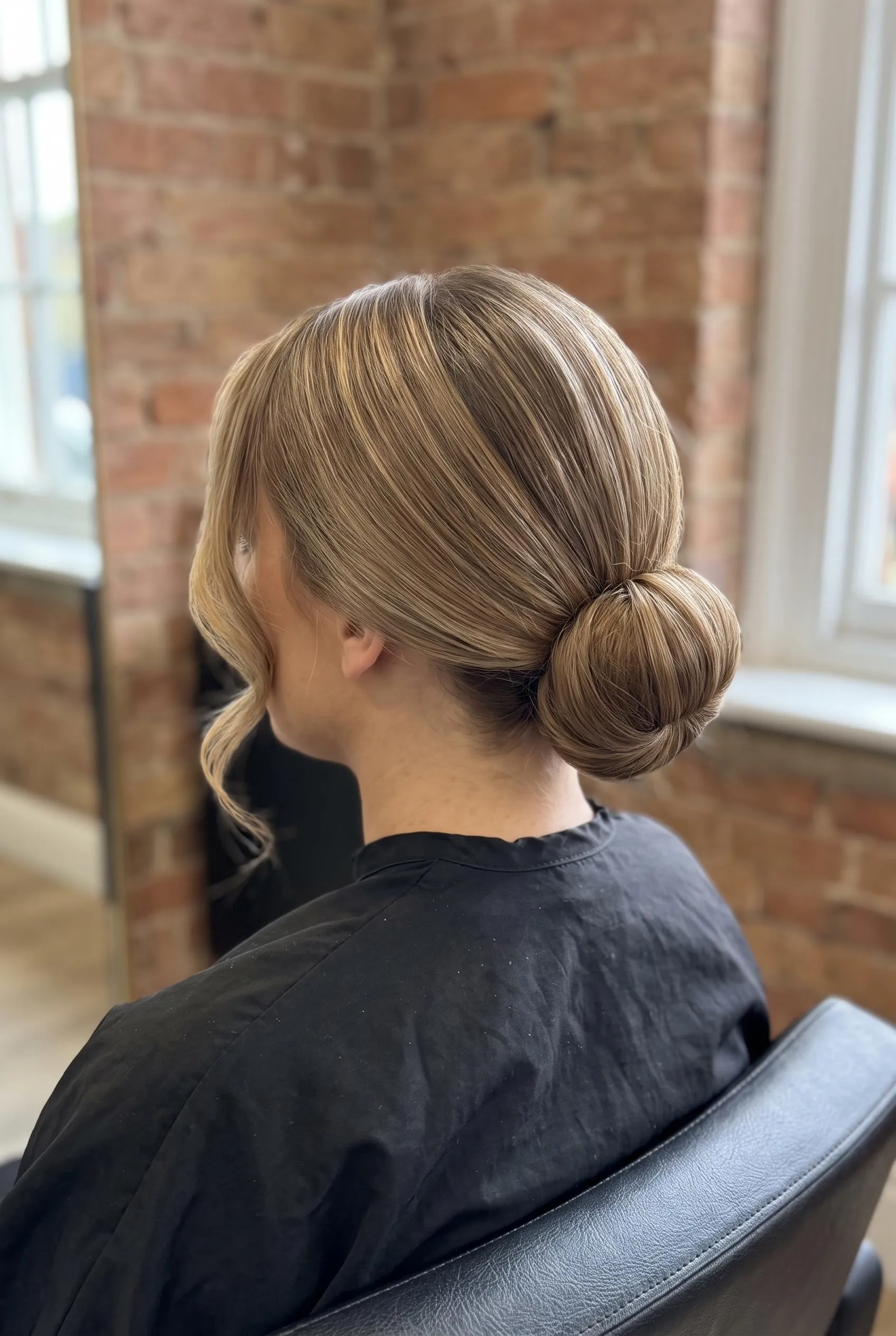 Sleek low bun with two curled face-framing pieces on bronde hair
