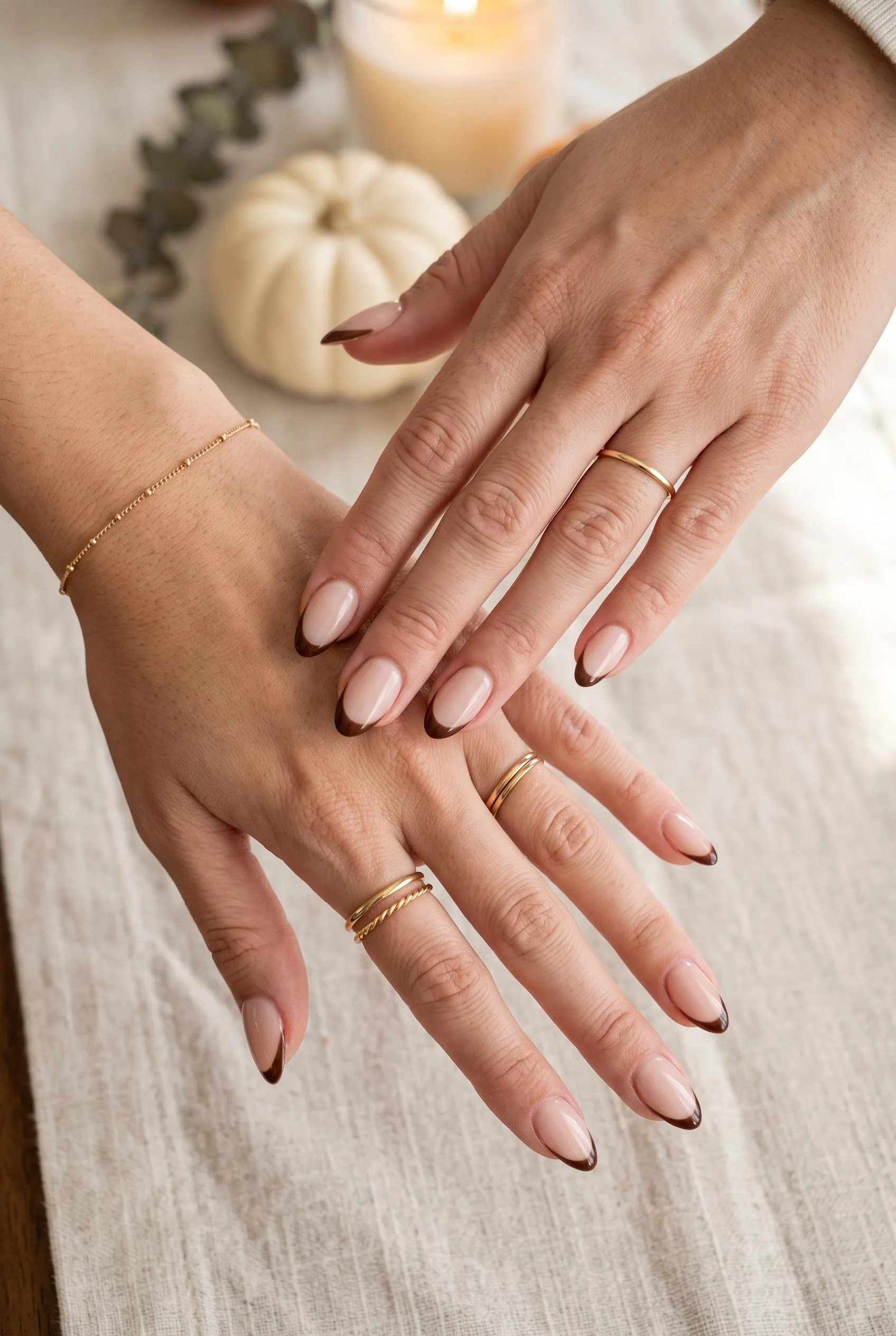 Almond nails with a sheer nude base and thin chocolate French tips on a Thanksgiving table