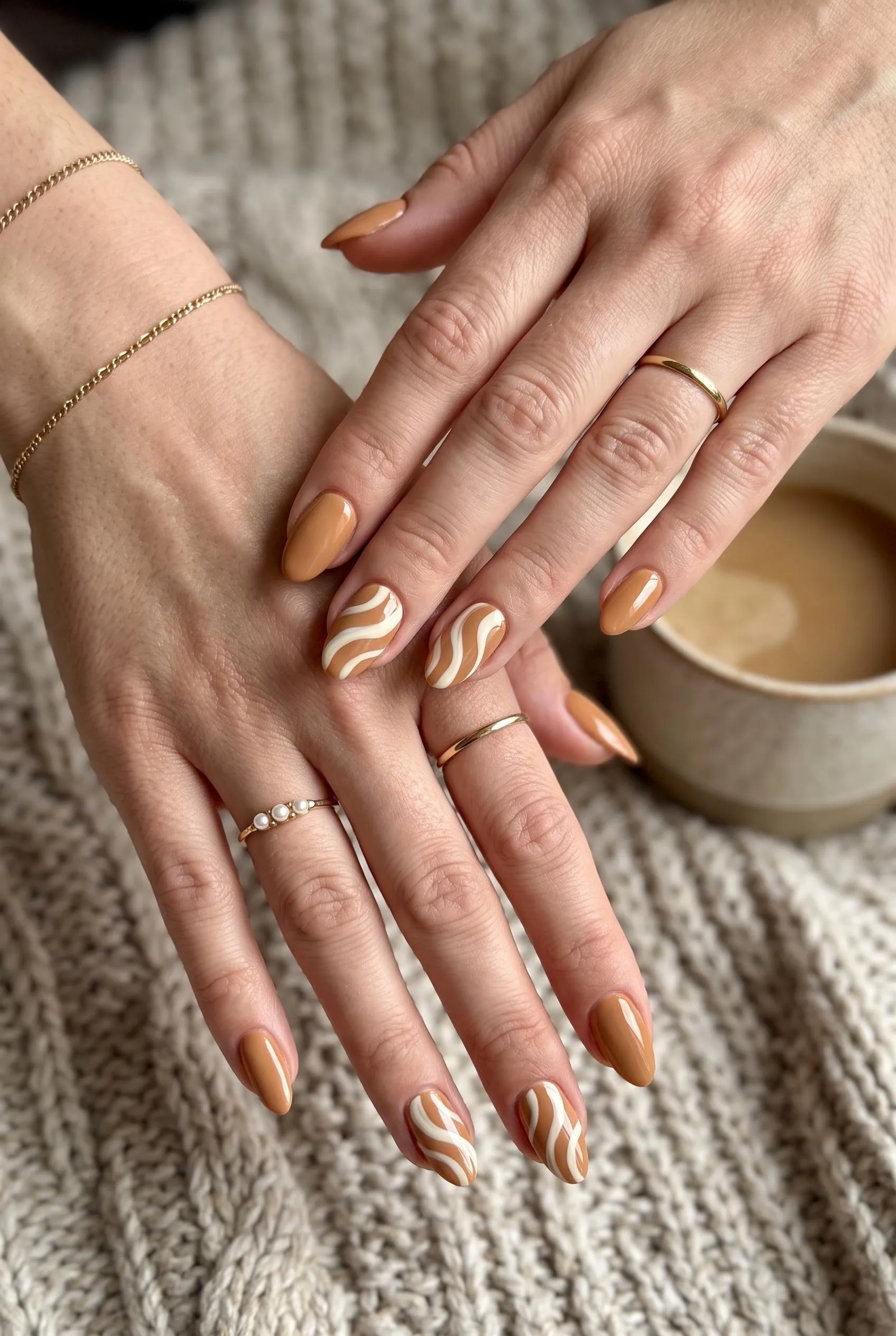 Caramel almond nails with cream swirls on the accent nails, holding near a coffee mug