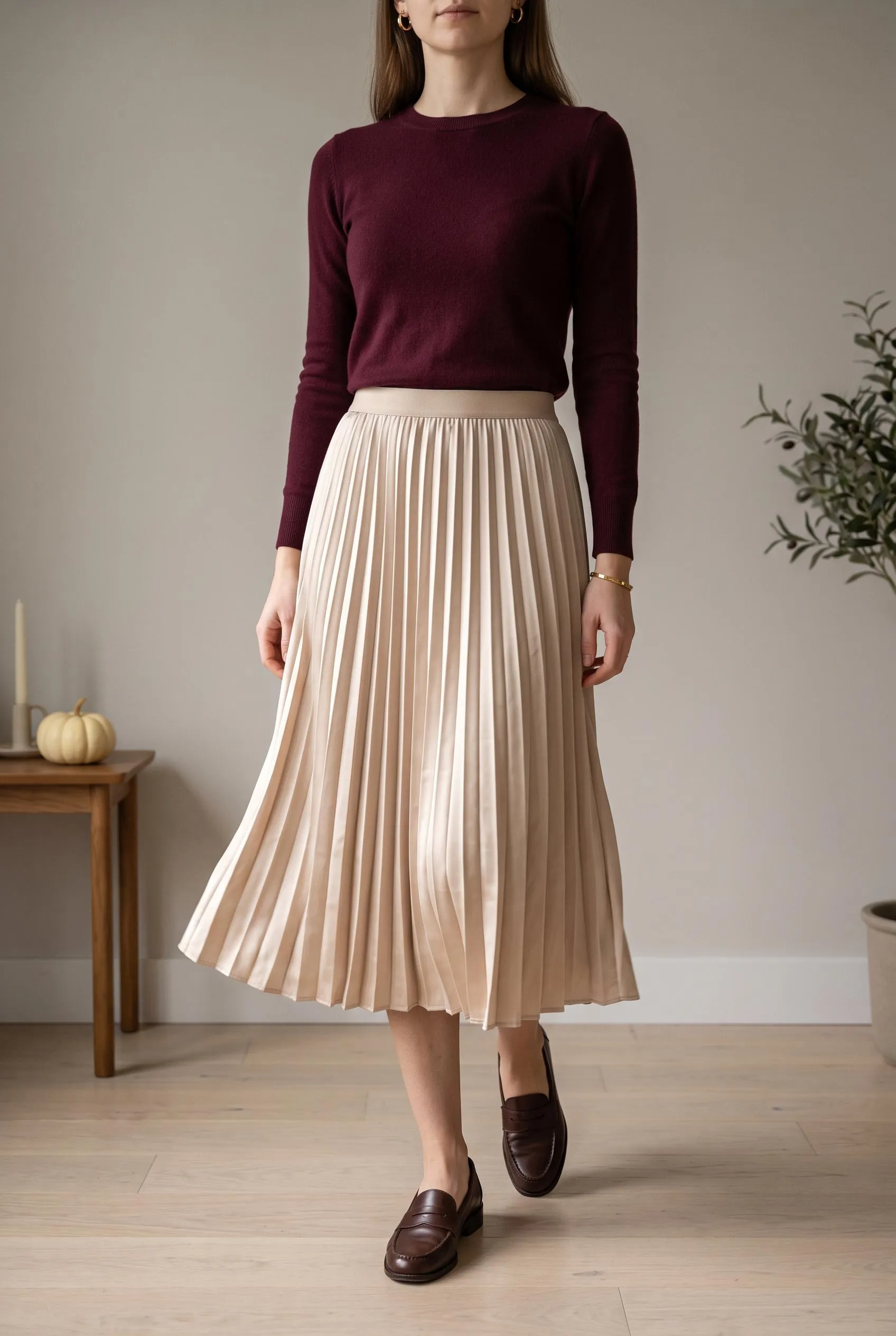 Burgundy fine-knit sweater tucked into a champagne pleated satin midi skirt with brown loafers