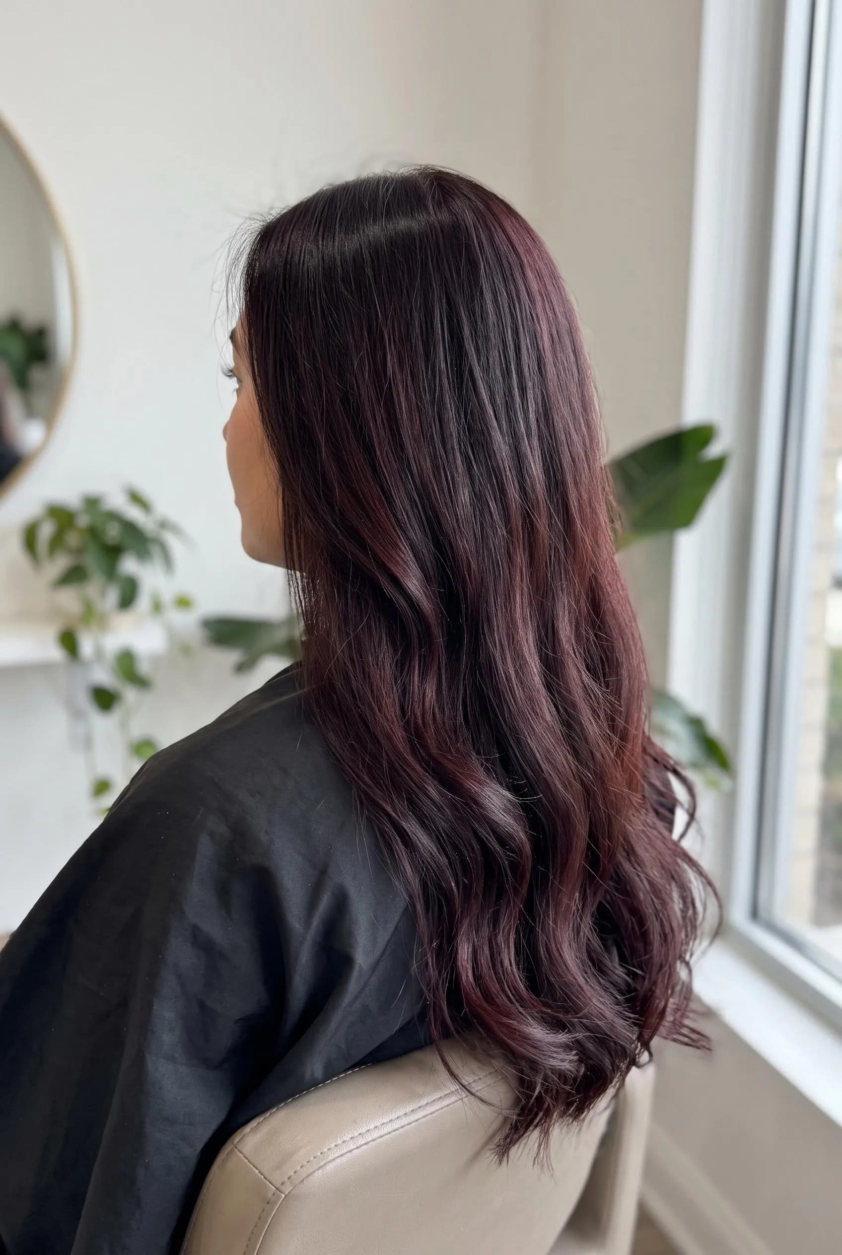 Long near-black hair with a black cherry red-violet glow, seen from behind in a salon