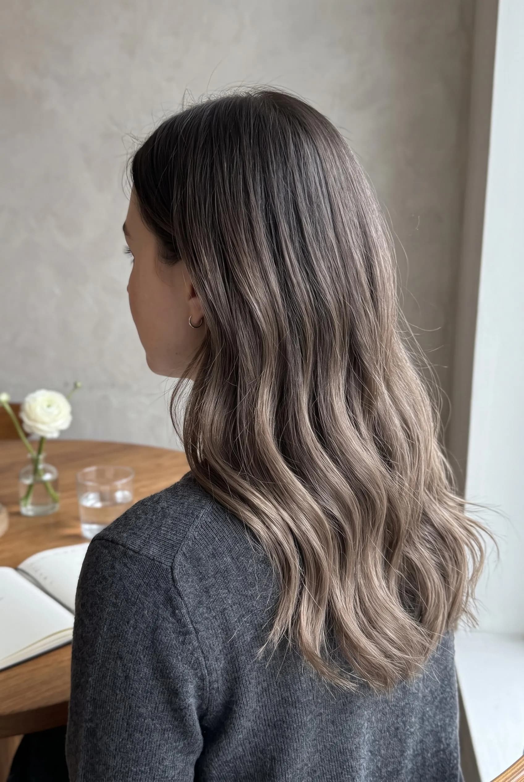 Smoky brunette balayage with ash-brown ends, seen from behind at a wooden table